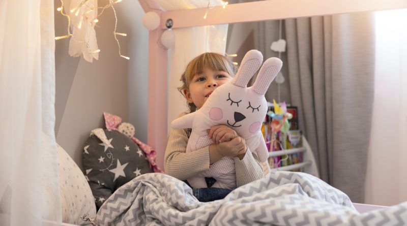 Dziewczynka siedzi w różowym łóżeczku domek dla dzieci, przytulając pluszowego królika w przytulnym pokoju
