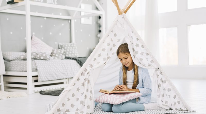 Dziewczynka czyta książkę obok łóżeczka dziecięcego domek w jasnym pokoju