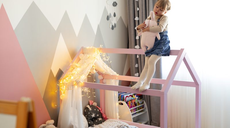 Dziecko bawi się na różowym łóżeczku domek dla dzieci ozdobionym światełkami